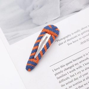 Handmade knitted hair clip with blue and orange stripes on stylish magazine background