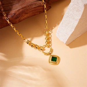 Detail shot of a gold-plated multi-layer chain necklace with a square green gemstone pendant