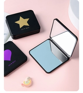 Detail of black folding makeup mirror with gold star patterns and double-sided lenses