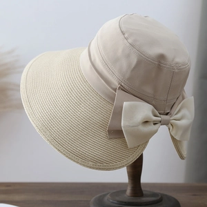 Elegant beige sun hat with straw brim and large bow accent on a wooden display stand