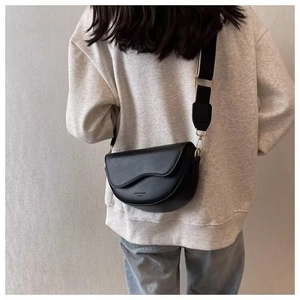 Rear view of a black saddle bag with an adjustable wide fabric strap on a model