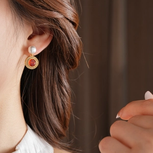 Détail d'une boucle d'oreille vintage dorée avec perle blanche et pierre orange sertie