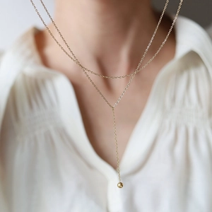 Close-up of elegant double-layered Y-shaped gold necklace with a polished bead pendant