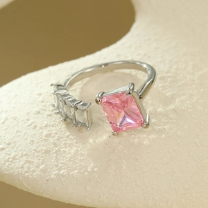 Close-up of silver open ring with pink rectangular gemstone on a textured surface