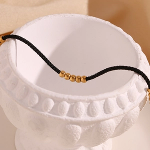 Close-up of black cord anklet with 18K gold-plated steel beads on a textured surface