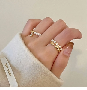Détail de bagues superposées plaquées or avec perles et breloques en zircon étincelant