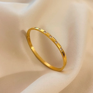 Detail shot of a minimalist gold bracelet featuring six square-set round zircons on fabric