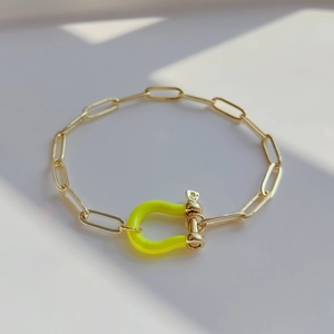 Detail view of gold paperclip chain bracelet featuring a vibrant yellow enamel shackle clasp