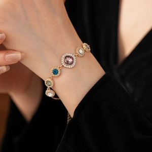 Close-up of a gold bracelet featuring multi-colored crystals on a model's wrist