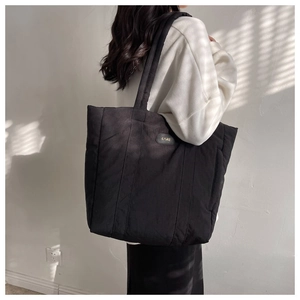 Side view of a model wearing a large quilted black nylon tote bag in natural window light