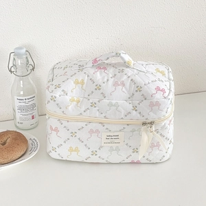Trousse à maquillage matelassée avec nœuds colorés et ruban de fermeture sur fond beige