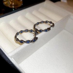 Detail of black metal hoop earrings with blue zircon inlays on white velvet