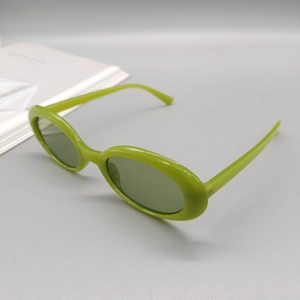 Detail view of avocado green oval frame sunglasses on a minimalist grey background
