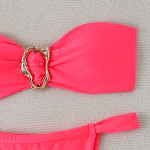 Flat lay of pink bandeau bikini with irregular gold metal buckle on white faux fur
