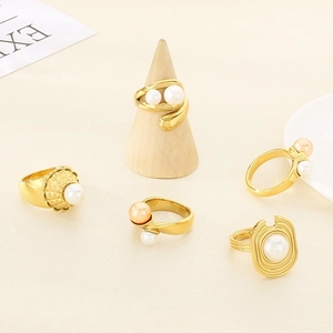 Elegant gold-tone geometric rings set with shell pearls on a minimalist wooden display stand