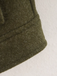 Detalle del dobladillo de chaqueta de lana verde oliva que muestra la textura y acabado