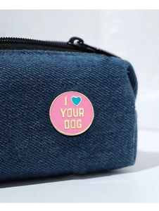 Detail of pink enamel brooch with gold 'I ♡ YOUR DOG' text on navy denim fabric