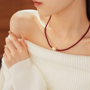 Gros plan d'un collier de perles rouges avec une perle dorée sur le cou d'un modèle