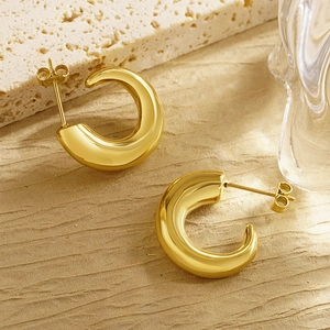 Detail of chunky gold C-shaped horn earrings with polished finish on beige texture