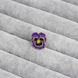 Close-up of purple and yellow pansy enamel brooch with gold trim on velvet fabric
