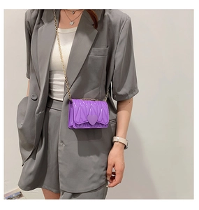 Detail of purple quilted silicone heart bag with golden chain strap on gray blazer