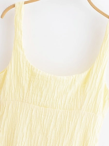 Detail of pale yellow dress featuring vertical tree bark pleated texture and thin straps