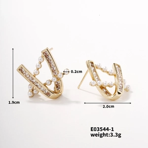 Detailed macro view of V-shaped gold earrings with white pearls and small rhinestones