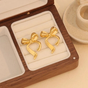 Elegant gold bow earrings made of stainless steel displayed on a wooden jewelry box