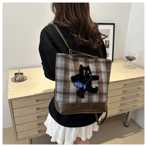 Plaid pattern tote backpack with plush black cat charm shown on model in home setting