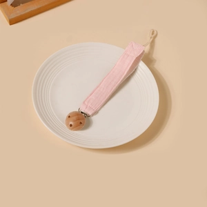 Détail de l'attache-tétine en coton rose avec clip en bois naturel sur assiette