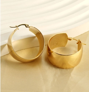 Vista macro de pendientes de aro anchos dorados sobre tela de seda beige elegante