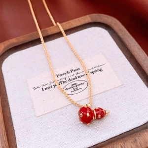 Macro view of 18k gold plated necklace featuring a red enamel gourd pendant on wood