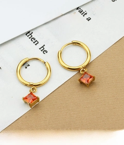 Close-up of gold titanium earrings with square orange zircon on white card background