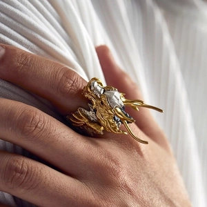 Detailed side view of vintage dragon ring in gold and silver finish on white fabric