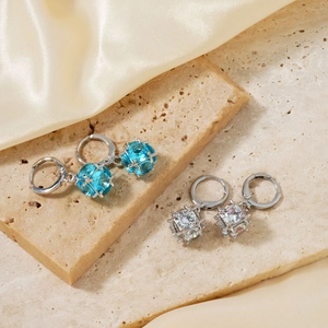 Detailed macro shot of blue spherical and white square gemstone stud earrings on beige stone