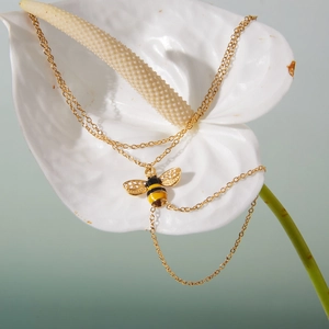 Nahaufnahme der goldenen Bienenkette mit Kristallen und Emaille auf einer weißen Blüte