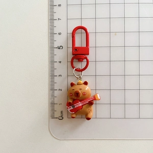 Size comparison of cute Capybara keychain with guitar on a grid measurement background