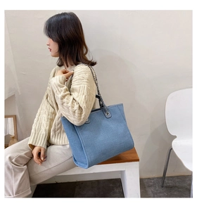 Modelo asiática con suéter beige y bolso tote de mezclilla azul con asa de cadena