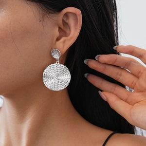 Close-up of silver geometric textured earrings featuring a spiral woven design on a model