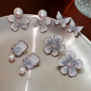 Detailed view of silver crystal butterfly flower and pearl earrings on a metal tray