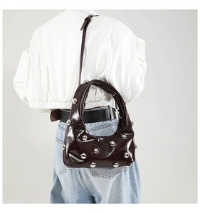 Close-up of shiny dark brown patent leather underarm bag with silver rivet details