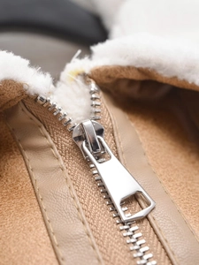 Close-up of silver metal zipper and soft white faux shearling lining on camel suede vest