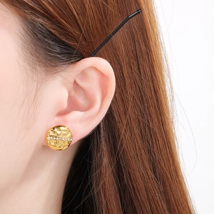 Close-up of golden round earrings with woven texture and a row of sparkling rhinestones
