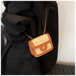 Detail of a woven straw shoulder bag with brown leather trim and golden chain strap
