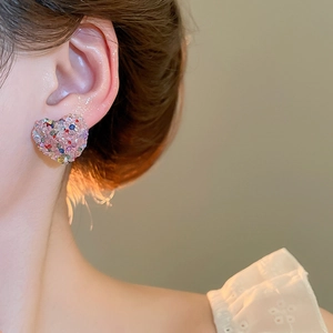 Close-up of a pink heart stud earring with sparkling crystals on woman ear
