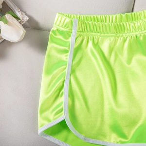 Detail view of neon green athletic shorts featuring white piping and satin finish texture