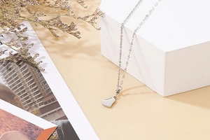 Silver heart pendant necklace displayed on white geometric props with dried flowers