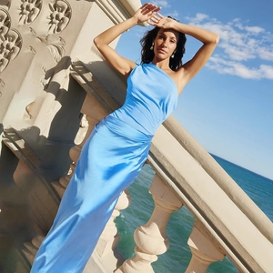 Détail d'une robe longue bleue à une épaule sur un mannequin face à l'océan bleu