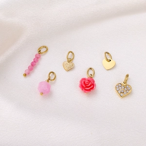 Detail of 6 gold heart charms with pink beads, roses, and crystals on white silk