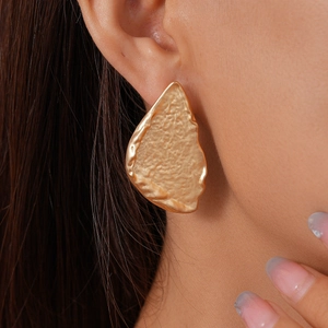 Close-up of golden irregular geometric stud earrings with textured hammer finish